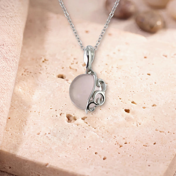 Collier pendentif quartz rose, modèle grand rond à volutes d'argent, sur sa chaîne, posé sur une dalle de travertin