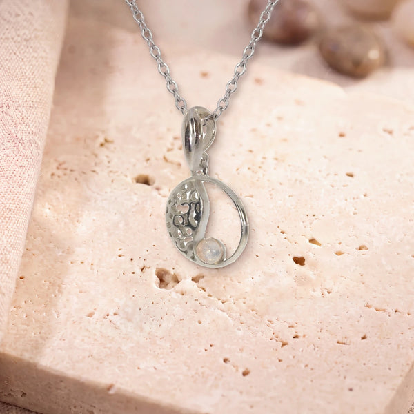 Petit pendentif quartz rose, modèle médaillon ajouré vintage, sur sa chaîne, posé sur une dalle de travertin