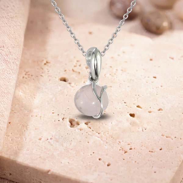 Pendentif quartz rose argent, modèle rond enlacé d'une liane d'argent, sur sa chaîne, posé sur une dalle de travertin