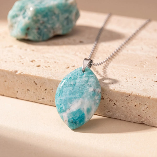 Pendentif pierre verte en amazonite, forme libre plate sur chaîne argentée, posé sur une dalle de travertin