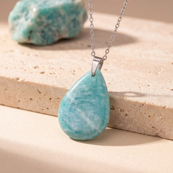 Pendentif pierre verte en amazonite, goutte plate polie sur chaîne argentée, posé sur du travertin beige