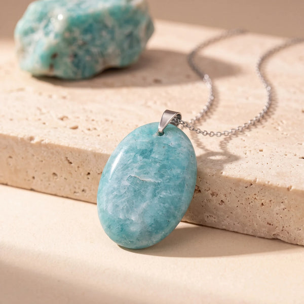 Pendentif pierre verte ovale en amazonite plate, bélière argentée, sur une dalle de travertin