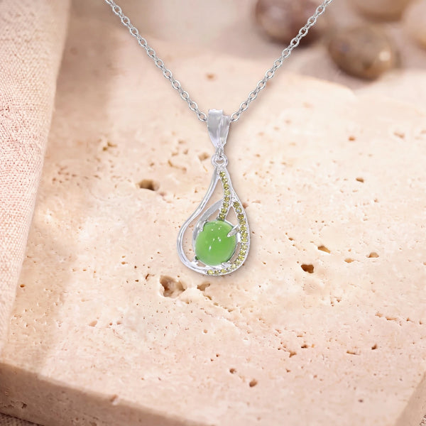Pendentif pierre de jade, modèle ovale dans une goutte d'argent ajourée, sur sa chaîne, posé sur une dalle de travertin