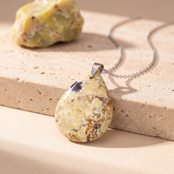 Pendentif pierre verte en opale naturelle, goutte plate opaque sur chaîne argentée, posée sur du travertin