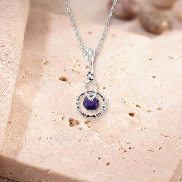 Collier améthyste homme, modèle rond au centre d'un anneau d'argent, sur sa chaîne, posé sur une dalle de travertin