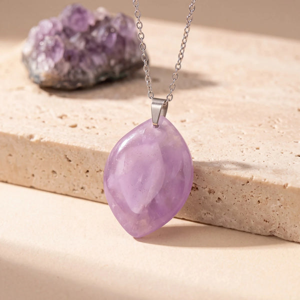 Pendentif pierre violette en améthyste, forme libre plate polie sur chaîne argentée, posée sur du travertin