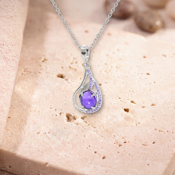 Pendentif pierre améthyste, modèle ovale dans une goutte d'argent ajourée, sur sa chaîne, posé sur une dalle de travertin