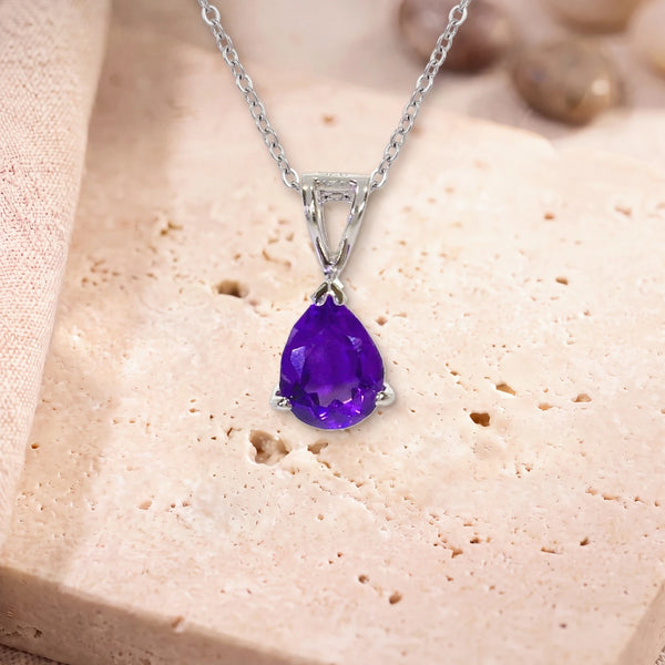 Collier goutte améthyste, modèle petite goutte facettée, sur sa chaîne, posé sur une dalle de travertin