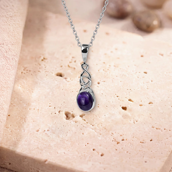 Pendentif améthyste argent, modèle ovale sous un entrelacs celtique, sur sa chaîne, posé sur une dalle de travertin