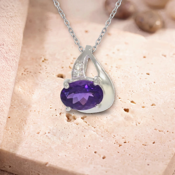 Pendentif améthyste véritable, modèle ovale facetté sur griffes, sur sa chaîne, posé sur une dalle de travertin
