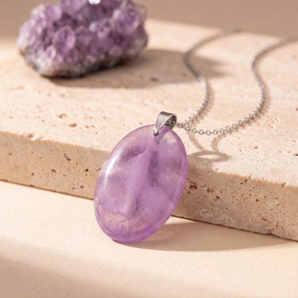 Pendentif pierre violette ovale en améthyste véritable, pierre plate polie posée sur du travertin