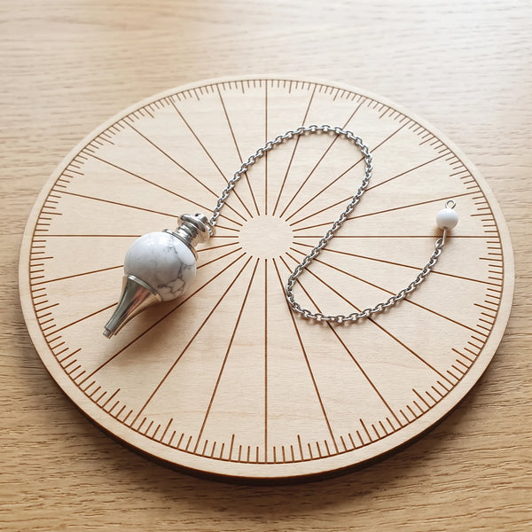Pendule blanc séphoroton en howlite posé sur une planche de radiesthésie en bois
