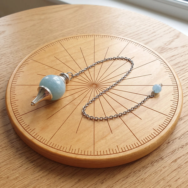 Pendule bleu séphoroton en aigue-marine posé sur une planche de radiesthésie en bois