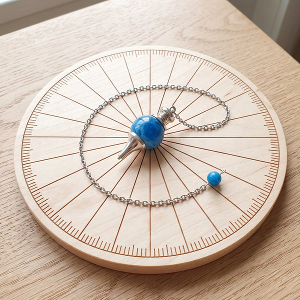 Pendule bleu séphoroton en apatite posé sur une planche de radiesthésie en bois