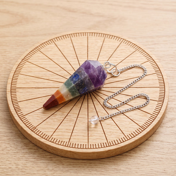 Pendule chakra multicolore facetté posé sur une planche de radiesthésie en bois