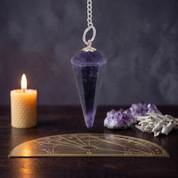 Pendule divinatoire en améthyste facettée, suspendu au-dessus d'une planche de radiesthésie à la lueur d'une bougie