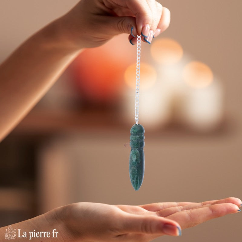 Pendule égyptien en aventurine verte oscillant au-dessus d'une planche de radiesthésie Fleur de Vie