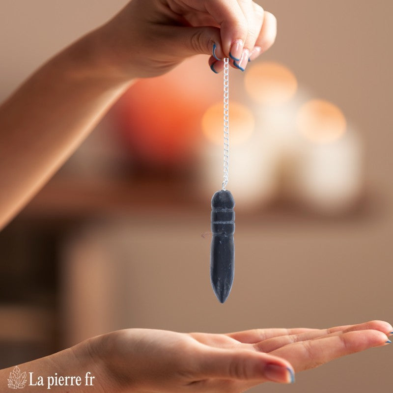 Pendule égyptien en shungite oscillant au-dessus d'une planche de radiesthésie Fleur de Vie