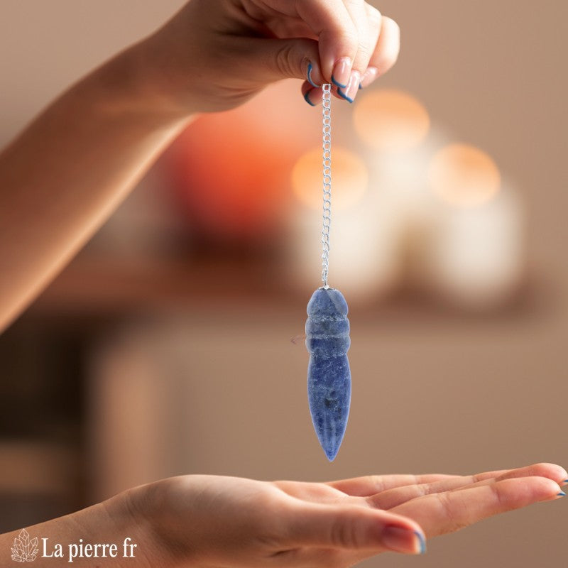 Pendule égyptien en sodalite oscillant au-dessus d'une planche de radiesthésie Fleur de Vie