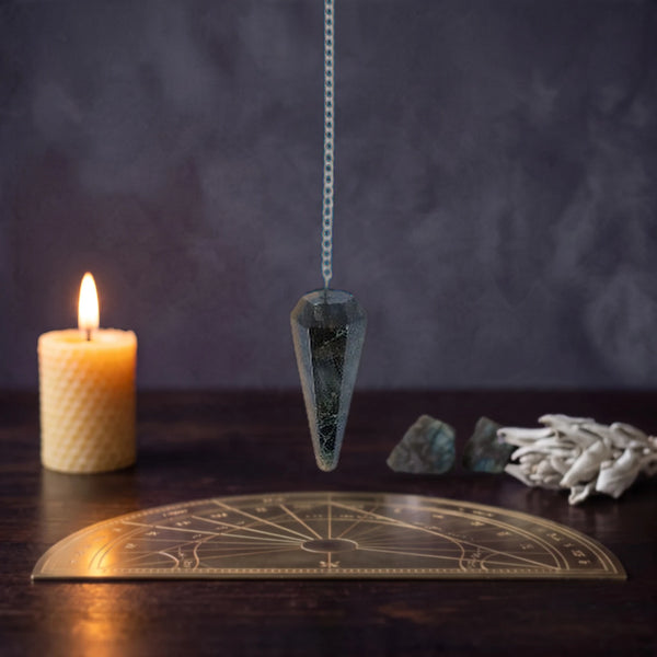 Pendule divinatoire en labradorite facettée au-dessus d'une planche de radiesthésie dorée
