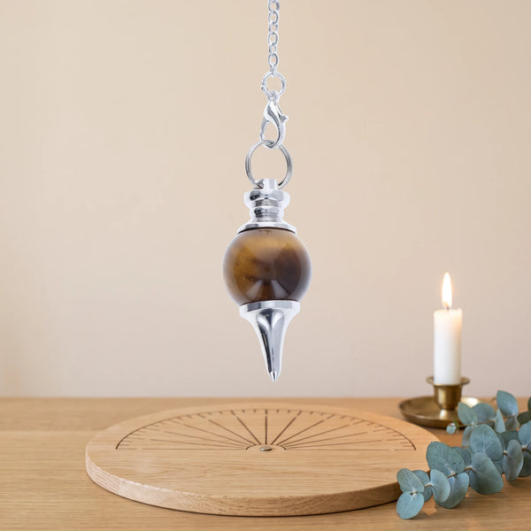 Pendule marron séphoroton en œil de tigre pour la radiesthésie, au-dessus d'une planche de radiesthésie