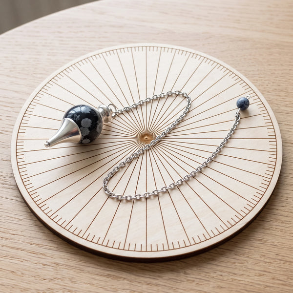 Pendule noir séphoroton en obsidienne neige posé sur une planche de radiesthésie en bois