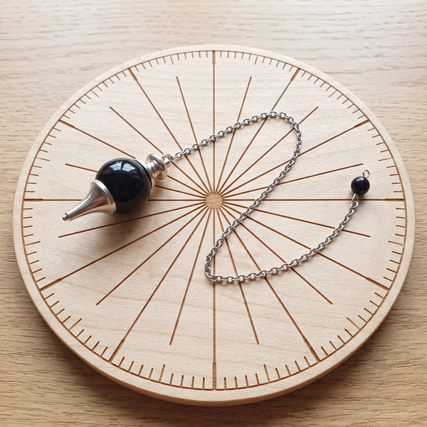 Pendule noir séphoroton en tourmaline noire posé sur une planche de radiesthésie en bois