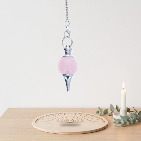 Pendule rose séphoroton en quartz rose pour la radiesthésie, au-dessus d'une planche de radiesthésie