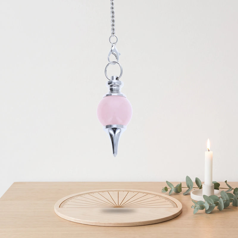 Pendule séphoroton en quartz rose oscillant au-dessus d'une planche de radiesthésie