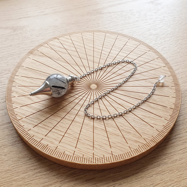 Pendule transparent séphoroton en quartz tourmaline posé sur une planche de radiesthésie en bois