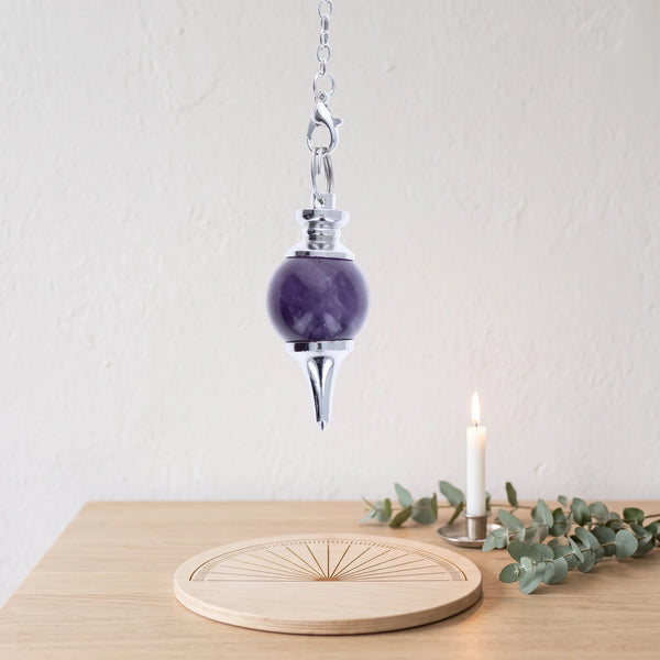 Pendule violet séphoroton en améthyste pour la radiesthésie, au-dessus d'une planche de radiesthésie