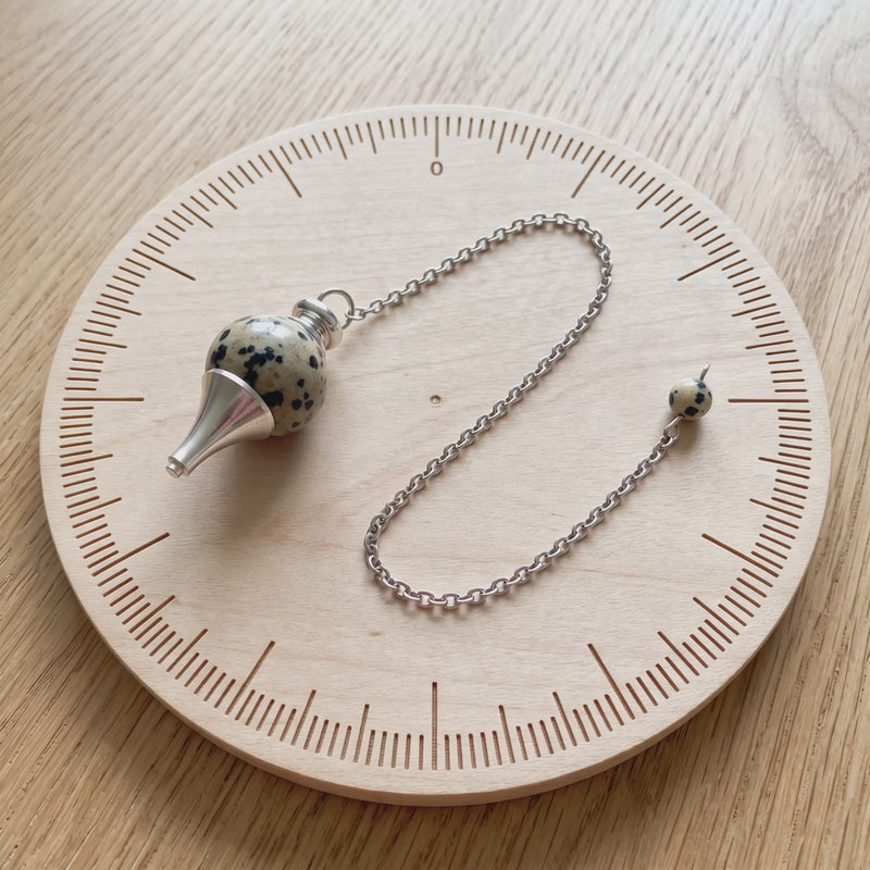 Pendule séphoroton en jaspe dalmatien sur une planche de radiesthésie
