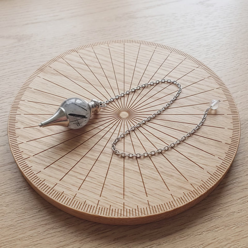 Pendule séphoroton en quartz tourmaline sur une planche de radiesthésie