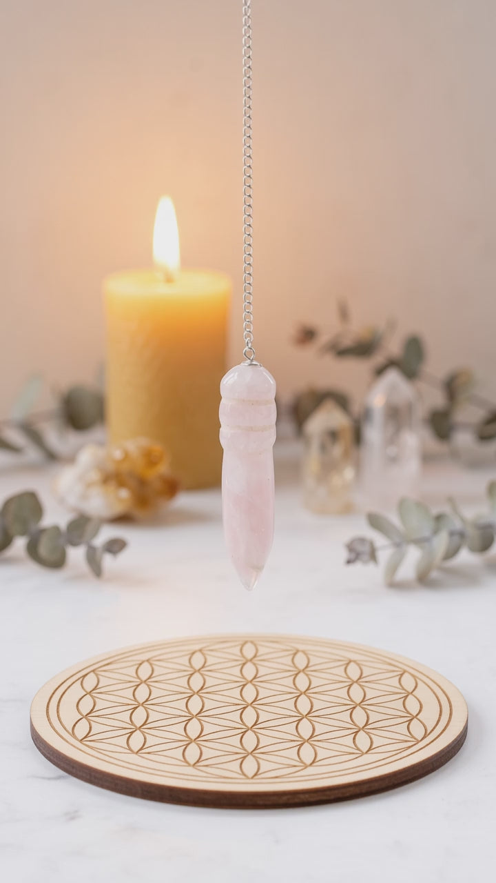 Pendule égyptien en quartz rose oscillant au-dessus d'une planche de radiesthésie Fleur de Vie