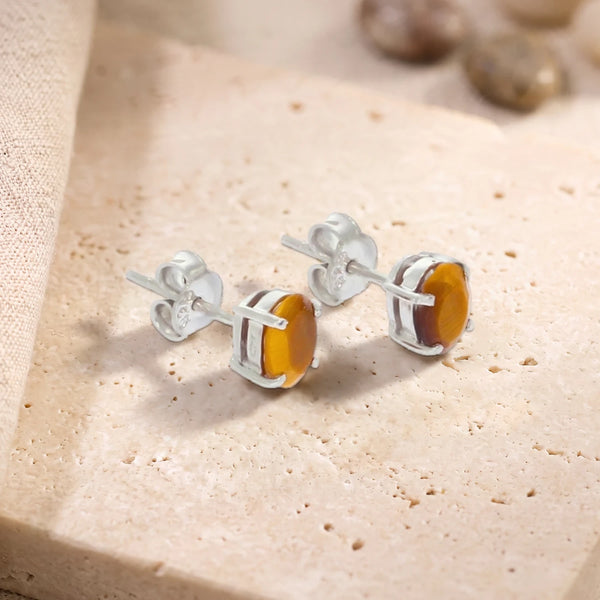Puces d'oreilles en œil de tigre ovale 7 x 5 mm sur argent 925 rhodié, paire posée sur une dalle de travertin