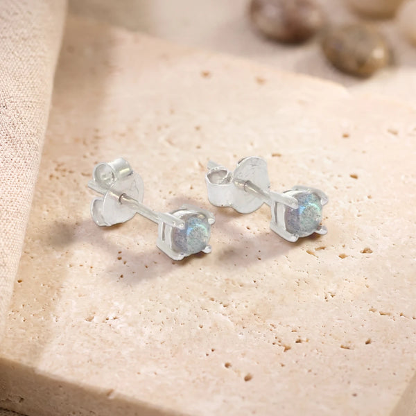 Puces d'oreilles en labradorite ronde 4 mm sur argent 925 rhodié, paire posée sur une dalle de travertin