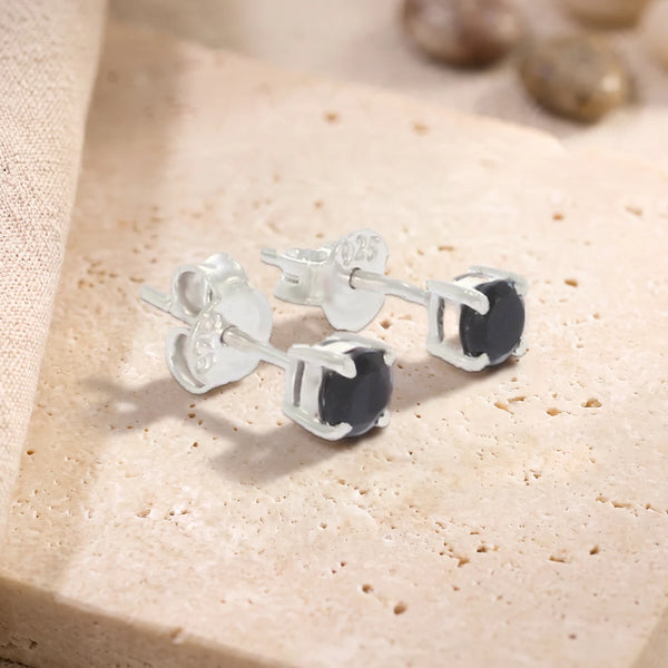 Puces d'oreilles en onyx noir rond 4 mm sur argent 925 rhodié, paire posée sur une dalle de travertin