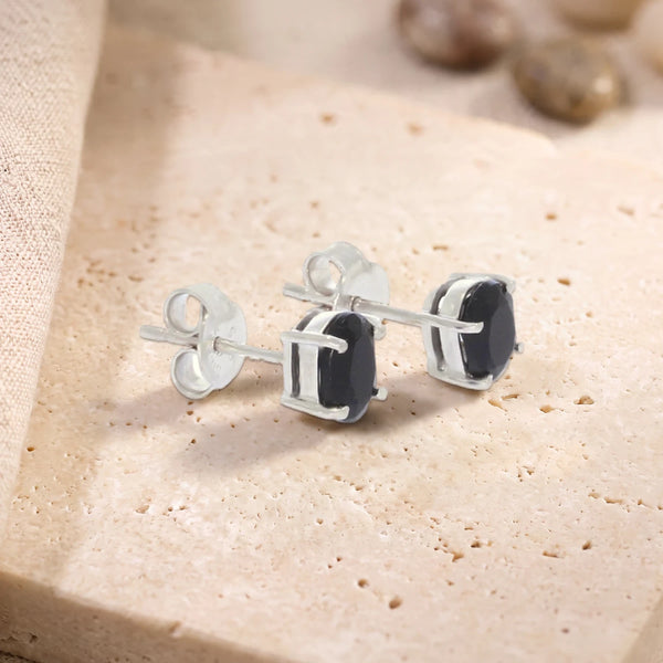 Puces d'oreilles en onyx noir ovale 7 x 5 mm sur argent 925 rhodié, paire posée sur une dalle de travertin