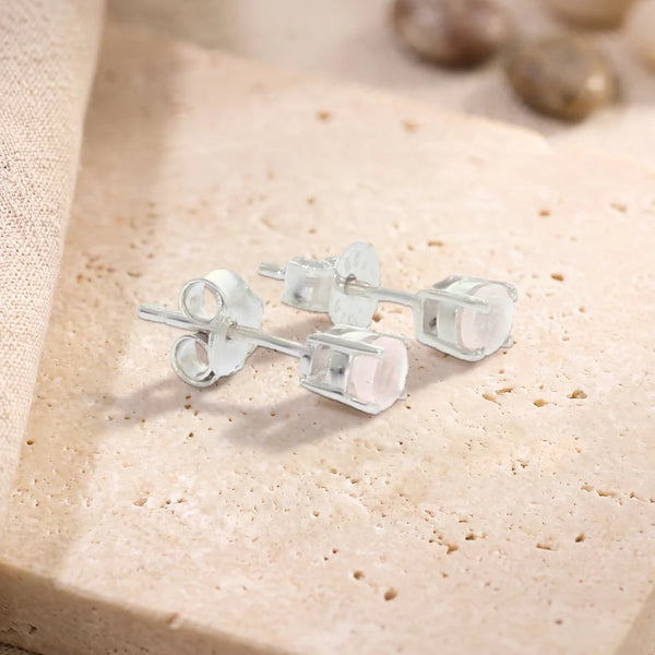 Puces d'oreilles en quartz rose rond 4 mm sur argent 925 rhodié, paire posée sur une dalle de travertin