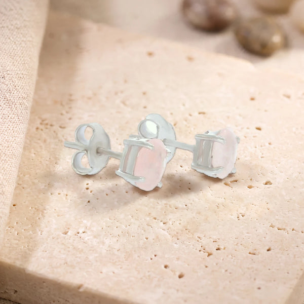 Puces d'oreilles en quartz rose ovale 7 x 5 mm sur argent 925 rhodié, paire posée sur une dalle de travertin