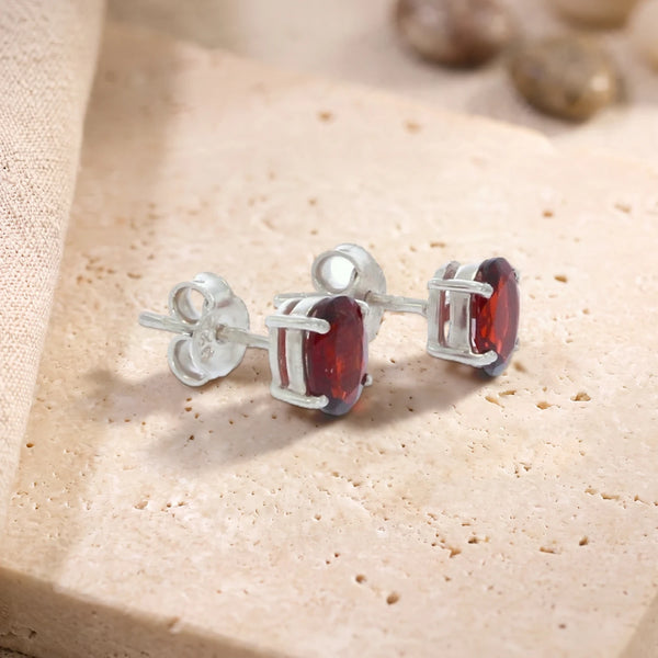 Puces d'oreilles en grenat ovale 7 x 5 mm sur argent 925 rhodié, paire posée sur une dalle de travertin