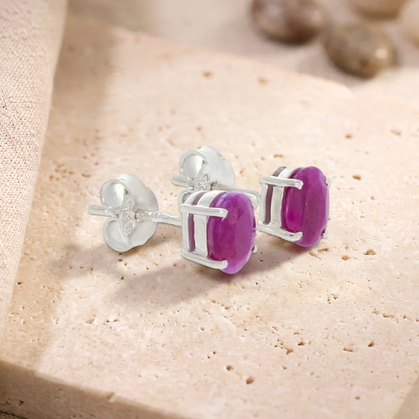 Puces d'oreilles en rubis ovale 7 x 5 mm sur argent 925 rhodié, paire posée sur une dalle de travertin