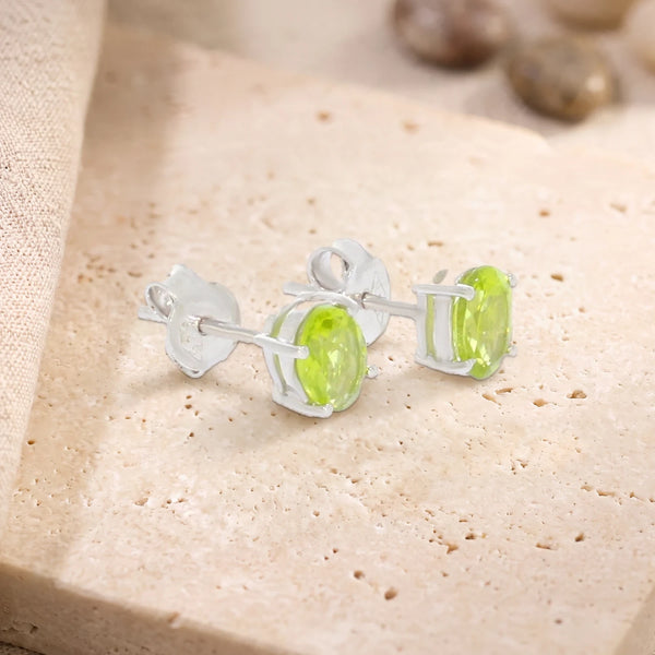 Puces d'oreilles en péridot ovale 7 x 5 mm sur argent 925 rhodié, paire posée sur une dalle de travertin