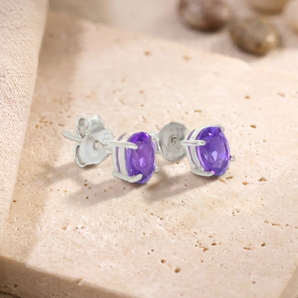 Puces d'oreilles en améthyste ovale 7 x 5 mm sur argent 925 rhodié, paire posée sur une dalle de travertin