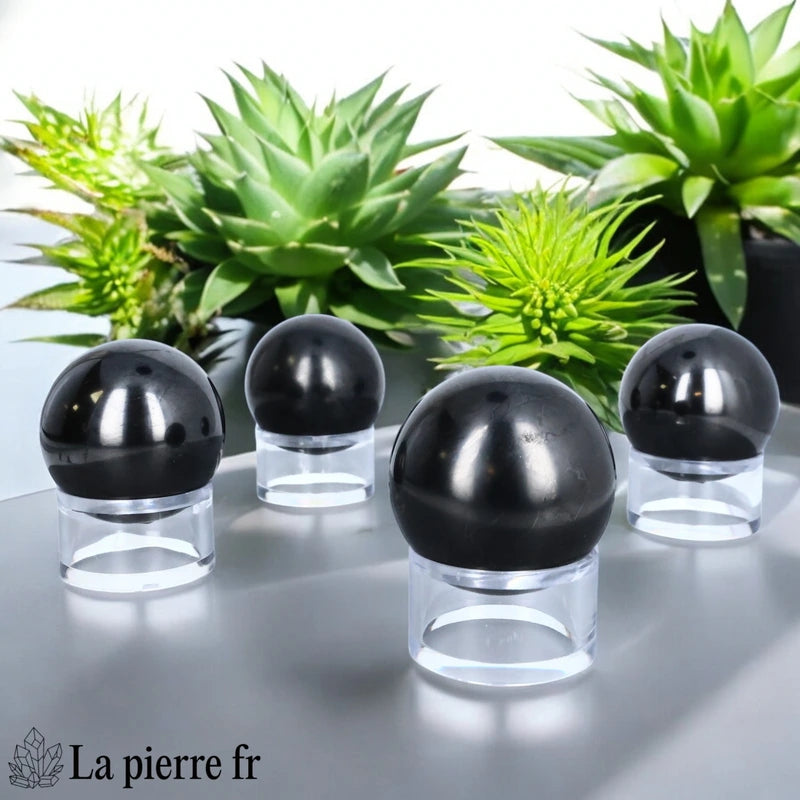 Sphère en Shungite posée sur un support transparent, pierre de lithothérapie parfaite pour neutraliser les énergies négatives.