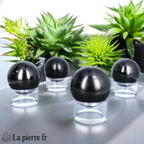 Sphère en Shungite posée sur un support transparent, pierre de lithothérapie parfaite pour neutraliser les énergies négatives.