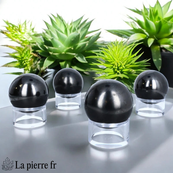 Sphère en Shungite posée sur un support transparent, pierre de lithothérapie parfaite pour neutraliser les énergies négatives.