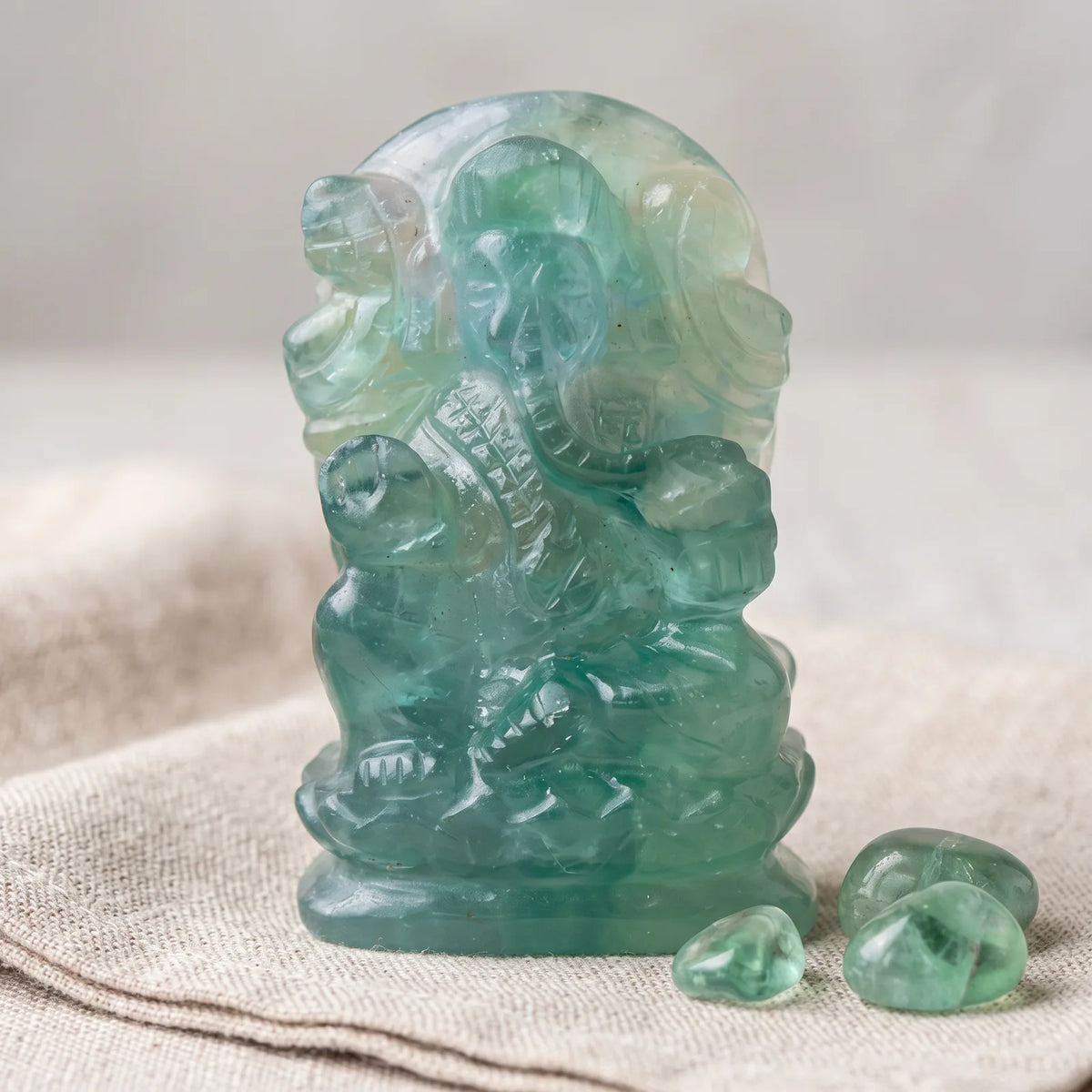 Statue de Ganesh en fluorine verte sur un lin naturel avec trois pierres roulées