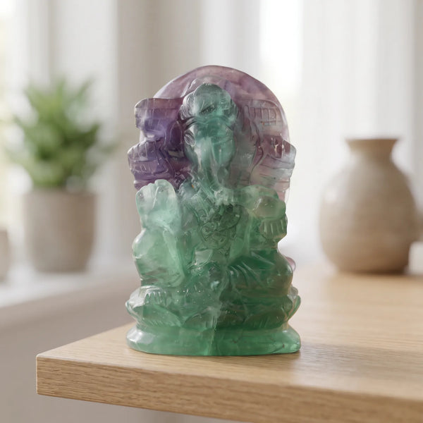 Statue Ganesh verte et violette en fluorite multicolore posée sur une étagère en bois clair