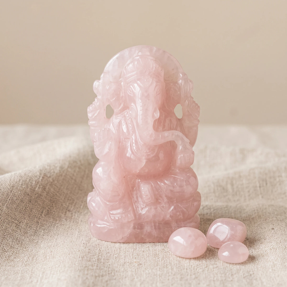 Statuette Ganesha en pierre de quartz rose sur un lin naturel avec trois pierres roulées